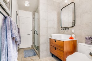 Un baño con inodoro blanco, tocador de madera con espejo y zona de ducha.