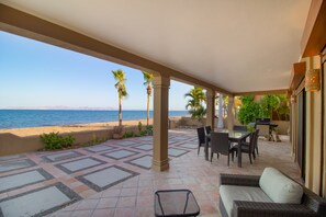 A covered patio with a view of the beach, outdoor furniture, and a grill area. - Rare Beachfront Steps to Sand/Paddleboards and Bikes (Loreto)