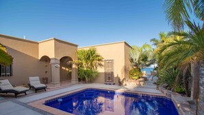 A swimming pool with lounge chairs, palm trees, and a building with arches. - Rare Beachfront Steps to Sand/Paddleboards and Bikes  (Loreto)