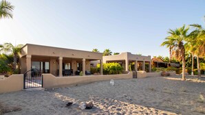 A hotel with a covered outdoor area, palm trees, and a sandy ground. - Rare Beachfront Steps to Sand/Paddleboards and Bikes  (Loreto)