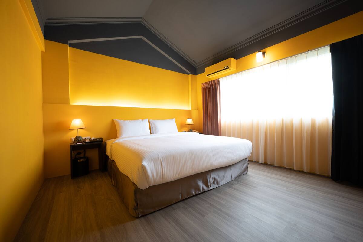 Quarto de hotel com cama grande, mesas de cabeceira e janela com cortinas.
