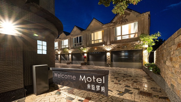A motel with a stone facade, multiple garage doors, and a welcome sign. - Yilan East Hotel (Jiaoxi)