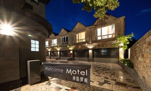 A motel with a stone facade, multiple garage doors, and a welcome sign. - Yilan East Hotel (Jiaoxi)
