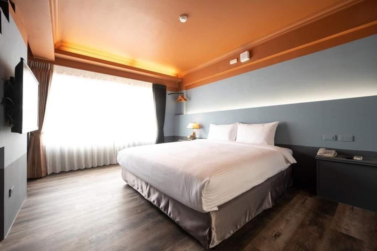Quarto de hotel com cama, mesa de cabeceira, luminária e televisão na parede.