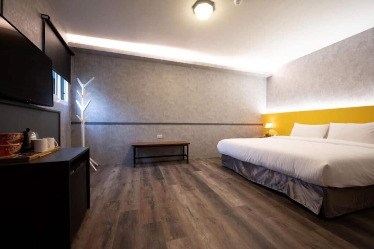 Quarto de hotel moderno com cama, mesa de cabeceira e um pequeno banco.