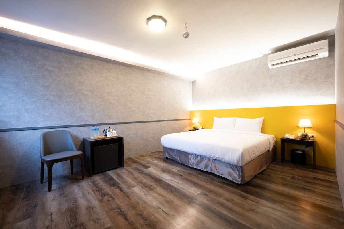 Quarto de hotel com cama, poltrona, mesa de cabeceira e aparelho de ar condicionado.