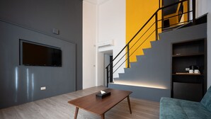 A modern living room with a wooden coffee table, a mounted TV, a staircase with a yellow accent wall, and a sofa. - Yilan East Hotel (Jiaoxi)