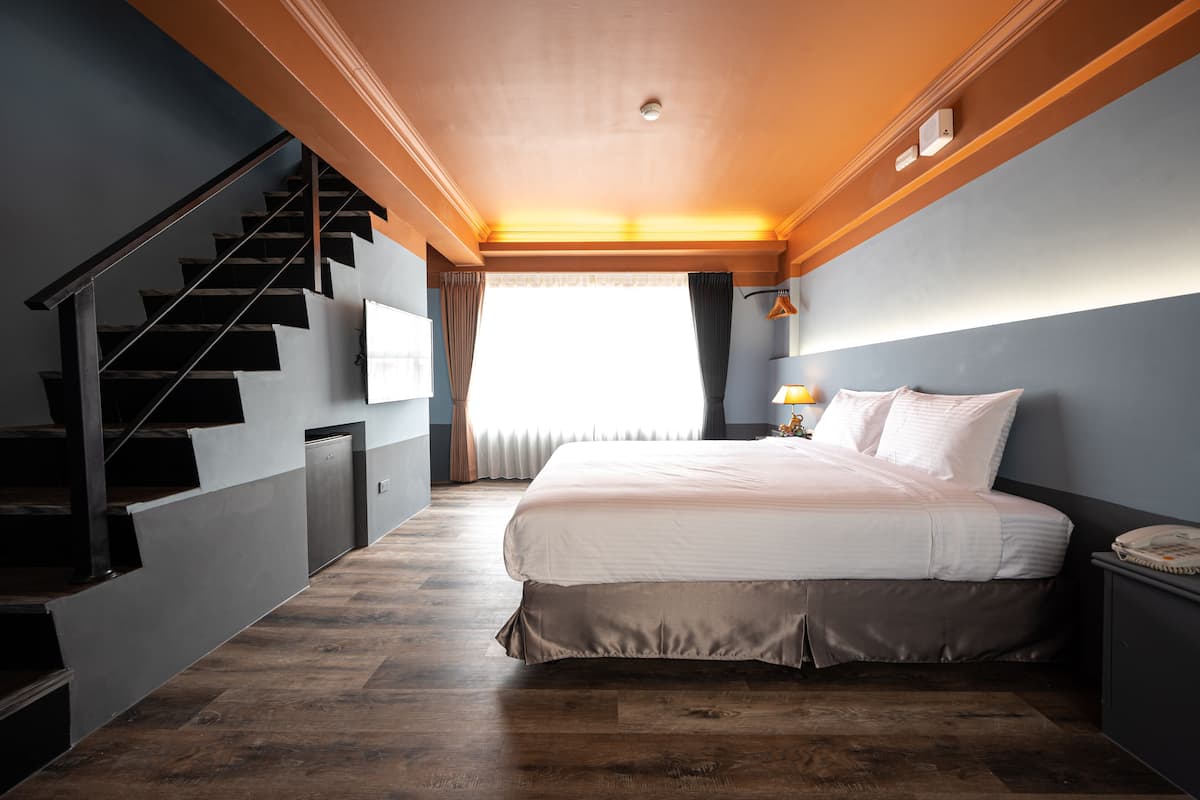Quarto com cama grande, escada de madeira e vista para o exterior.