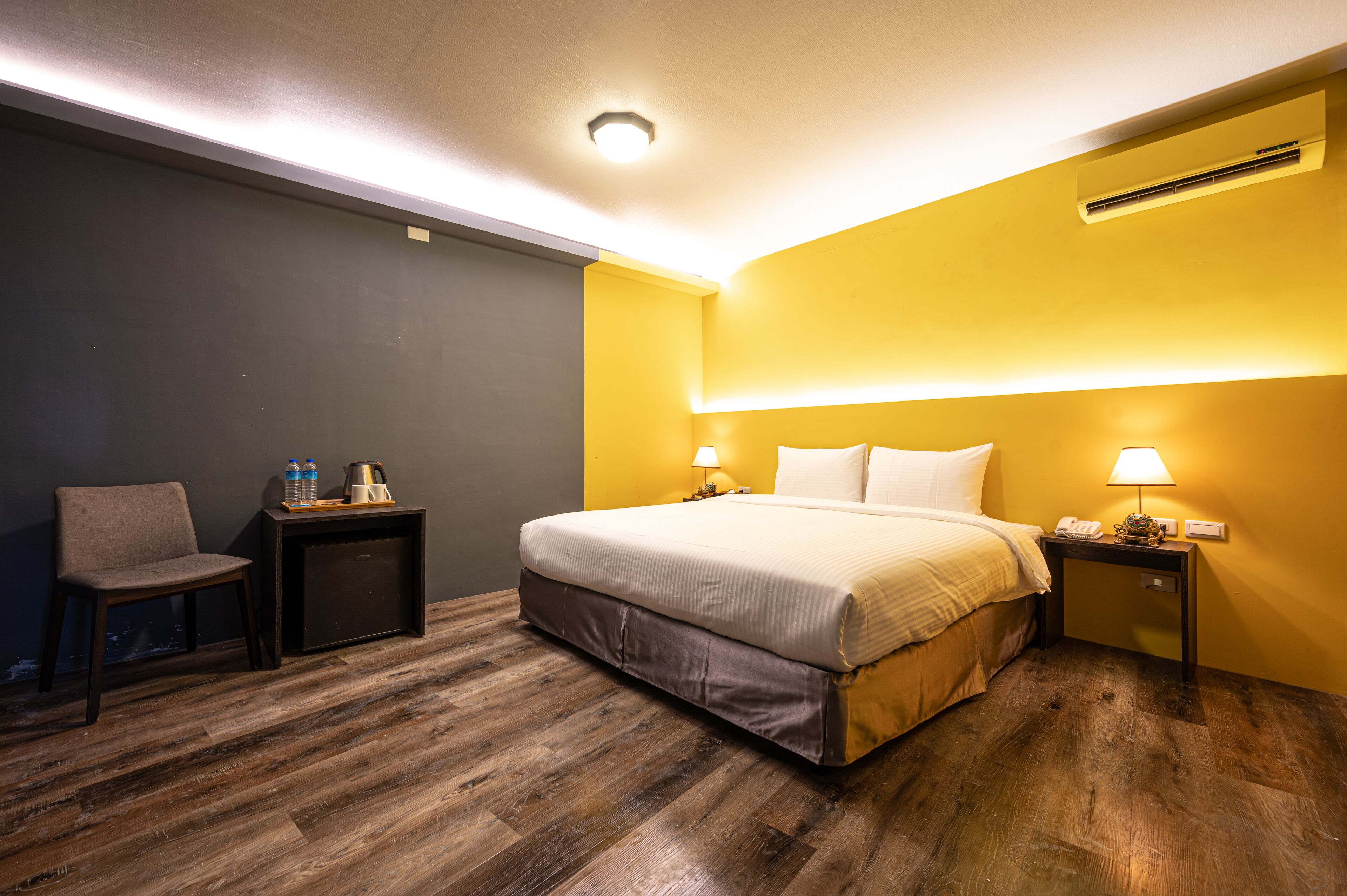 A hotel room with a bed, a chair, a nightstand, and a bedside table.