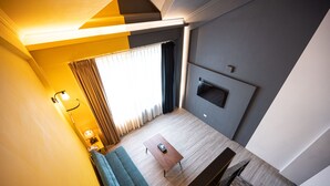 A modern hotel room with a wooden floor, a sofa, a coffee table, a TV mounted on the wall, and a window with curtains. - Yilan East Hotel (Jiaoxi)