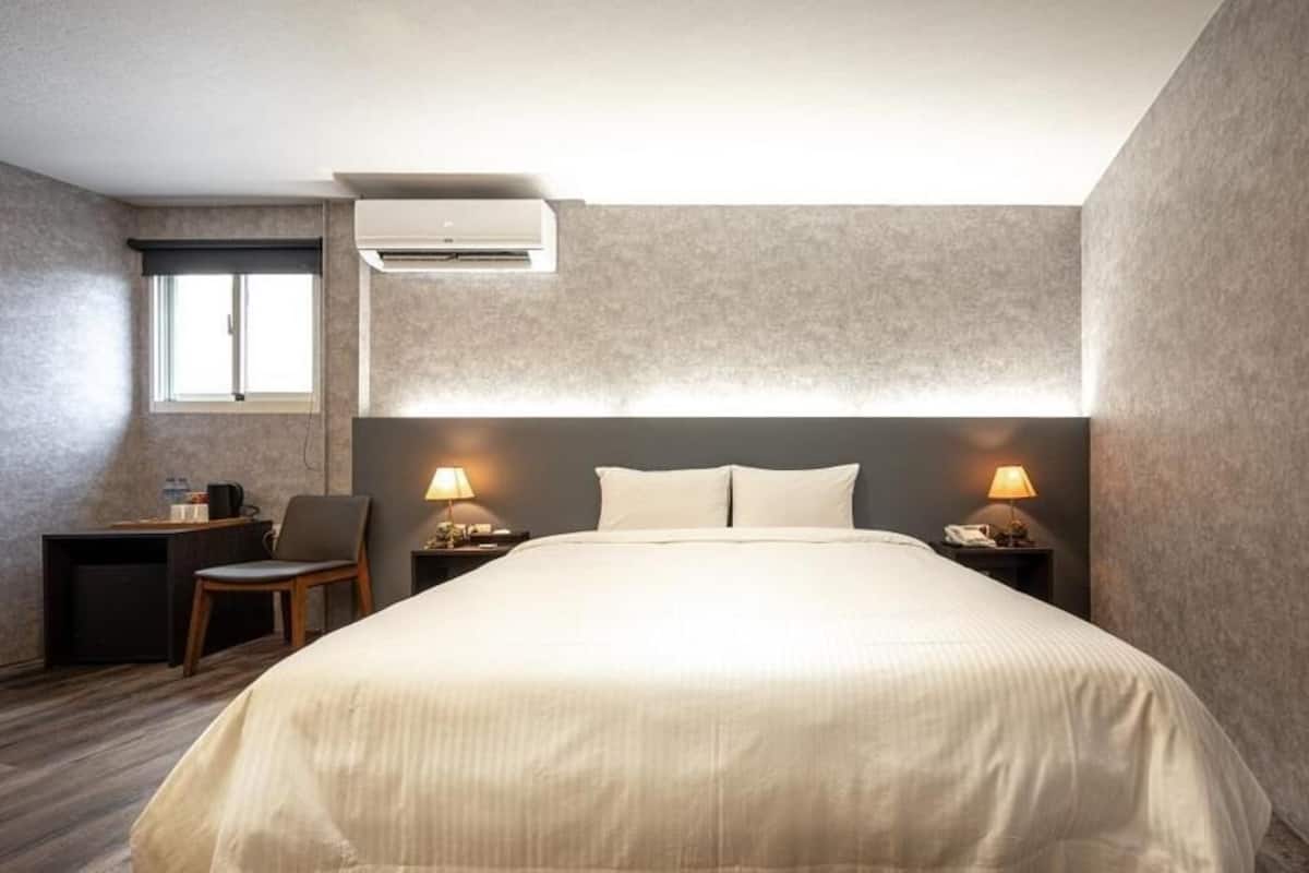 Quarto com cama, duas luminárias de cabeceira, escrivaninha com cadeira e ar condicionado.