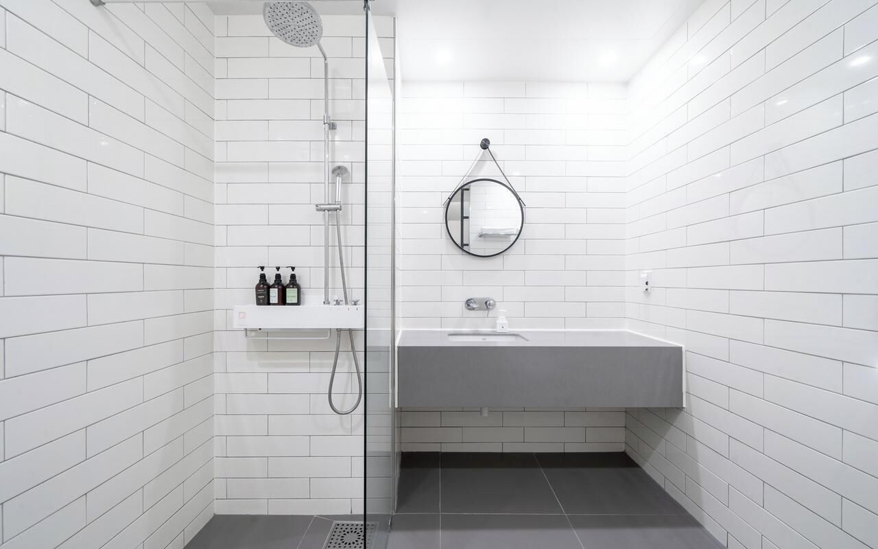 A modern bathroom with white tiled walls, a grey sink, a mirror, and a shower area.