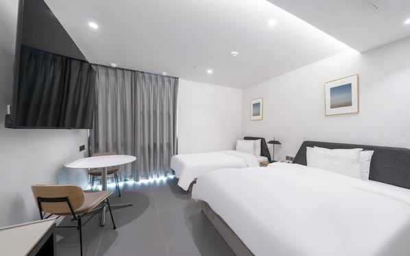 Una habitación de hotel moderna con dos camas, un escritorio, una silla, una mesa redonda y un televisor montado en la pared.