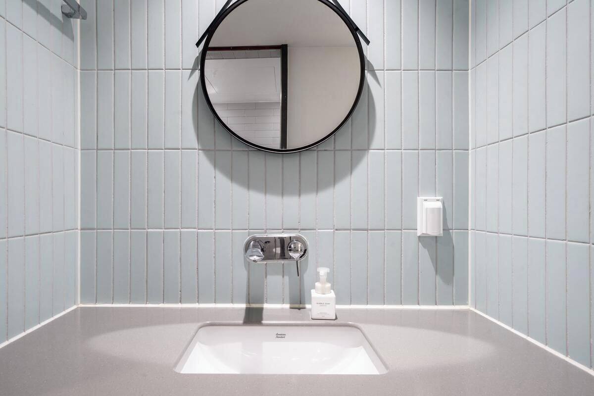 Un baño con un espejo redondo, un lavamanos y un dispensador de jabón.