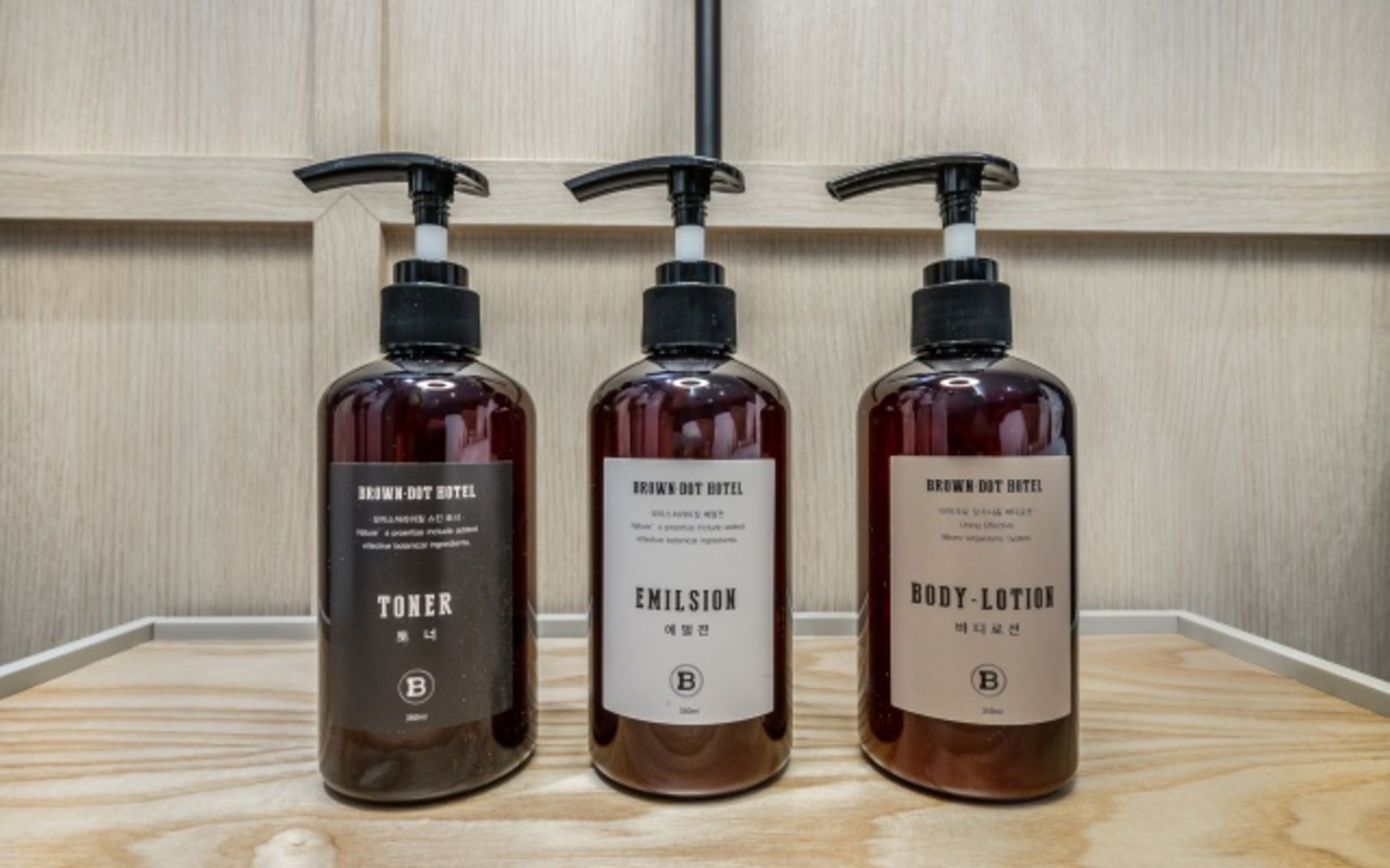 Three bottles of Brown Dot Hotel products: toner, emulsion, and body lotion.