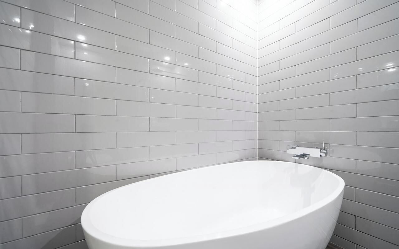 A modern bathroom with white tiles, a freestanding bathtub, and a wall-mounted faucet.