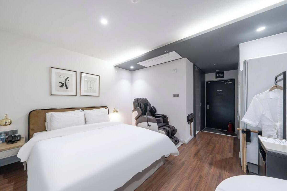 Habitación de hotel con una cama grande, una silla de masaje, un escritorio con silla y una puerta con el número 703.