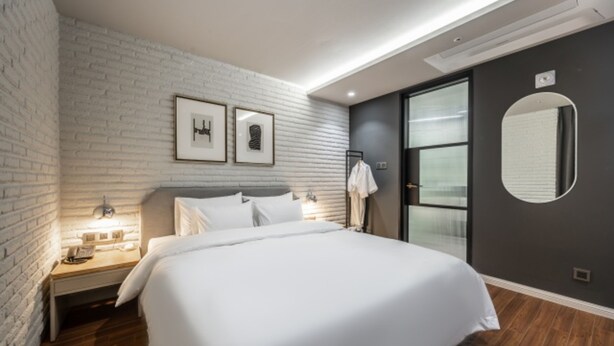 A modern hotel room with a brick wall, a large bed, a wardrobe, and a mirror. - Brown Dot Hotel Busan Sajik Stadium (Busan)