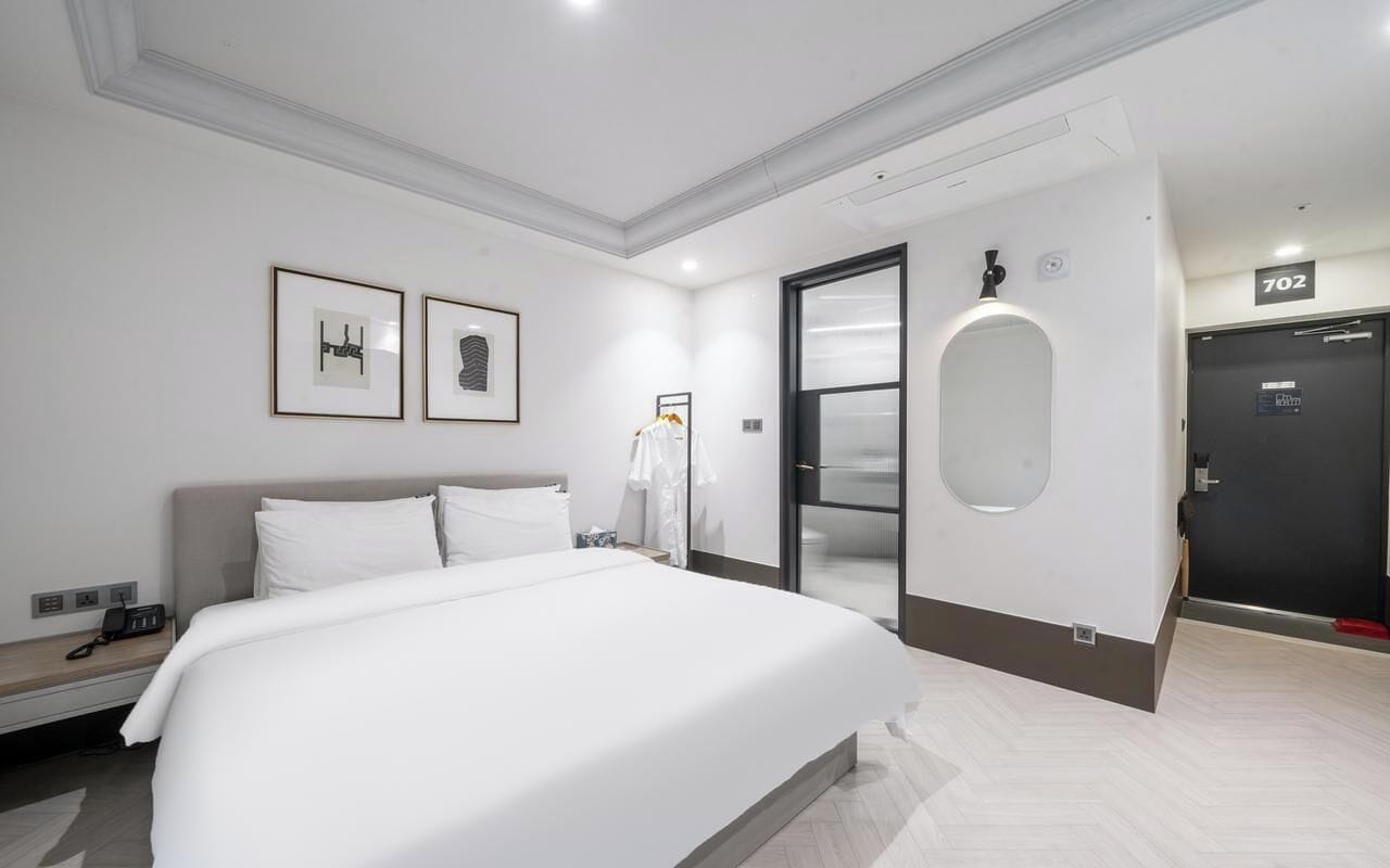 A modern hotel room with a large bed, a bedside table with a phone, a mirror, and framed pictures on the wall.
