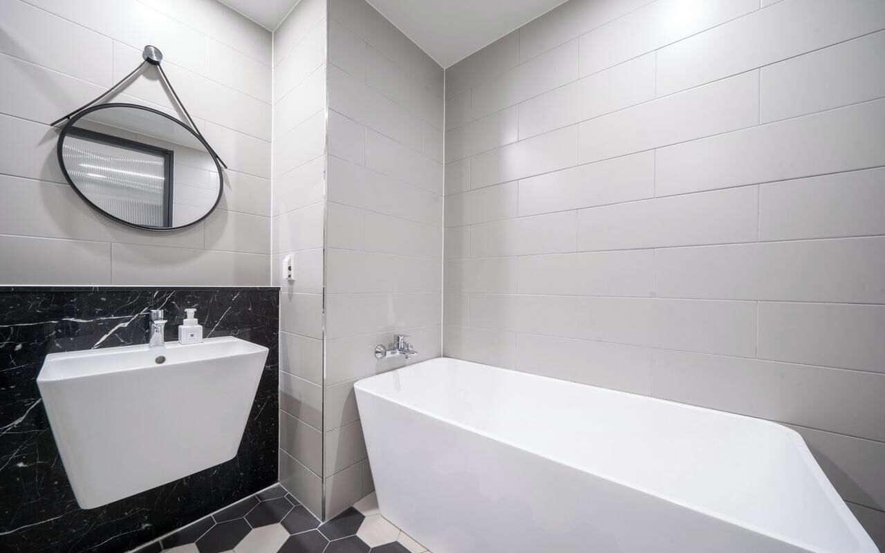 Un baño moderno con una bañera independiente, un lavabo de pared y un espejo redondo.