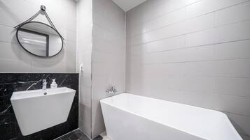 Un baño moderno con una bañera independiente, un lavabo de pared y un espejo redondo.