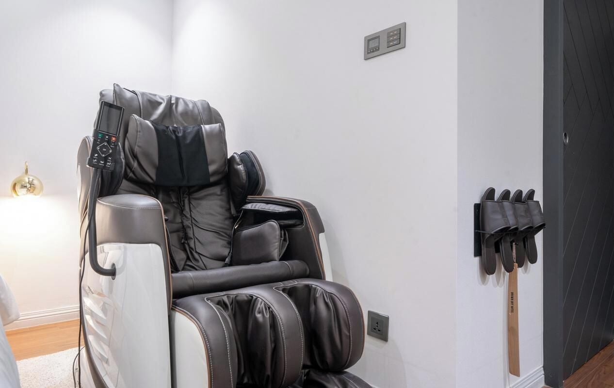 A massage chair with a control panel, a wall-mounted massage gun rack, and a wooden door.