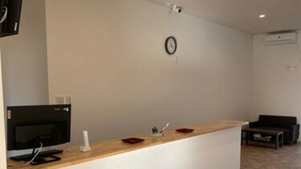 A reception area with a wooden counter, a clock, and a television on the left. - Hotel46 (Hashimoto)