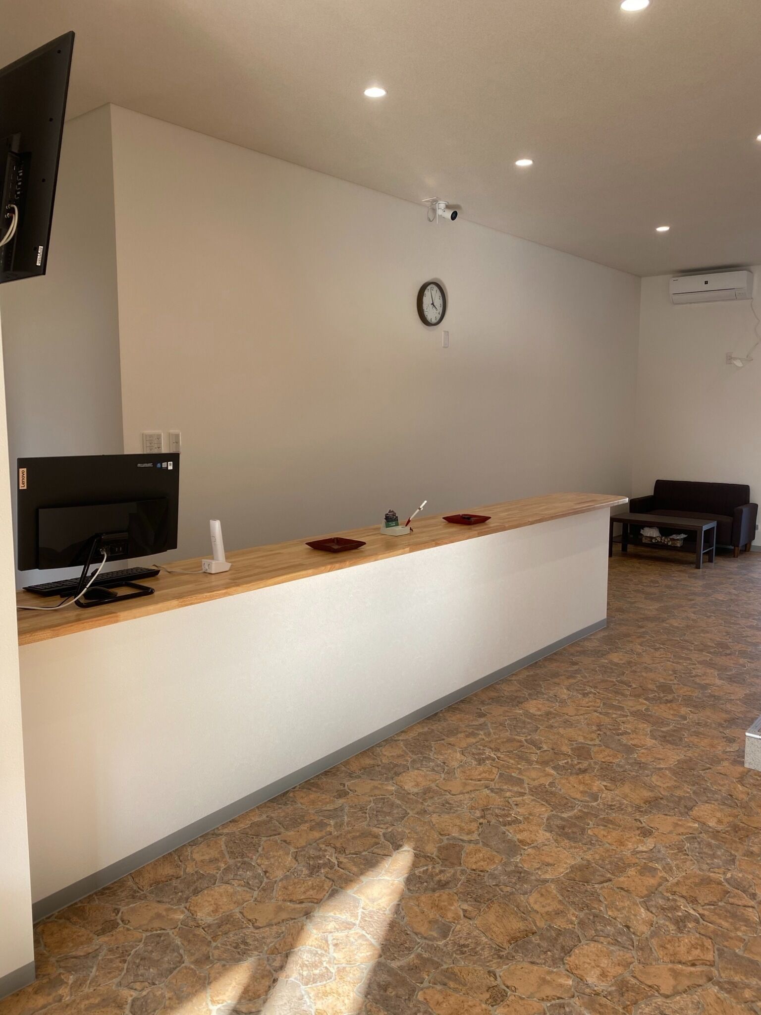 A reception desk with a flat-screen TV, a clock, and an air conditioning unit on the wall.