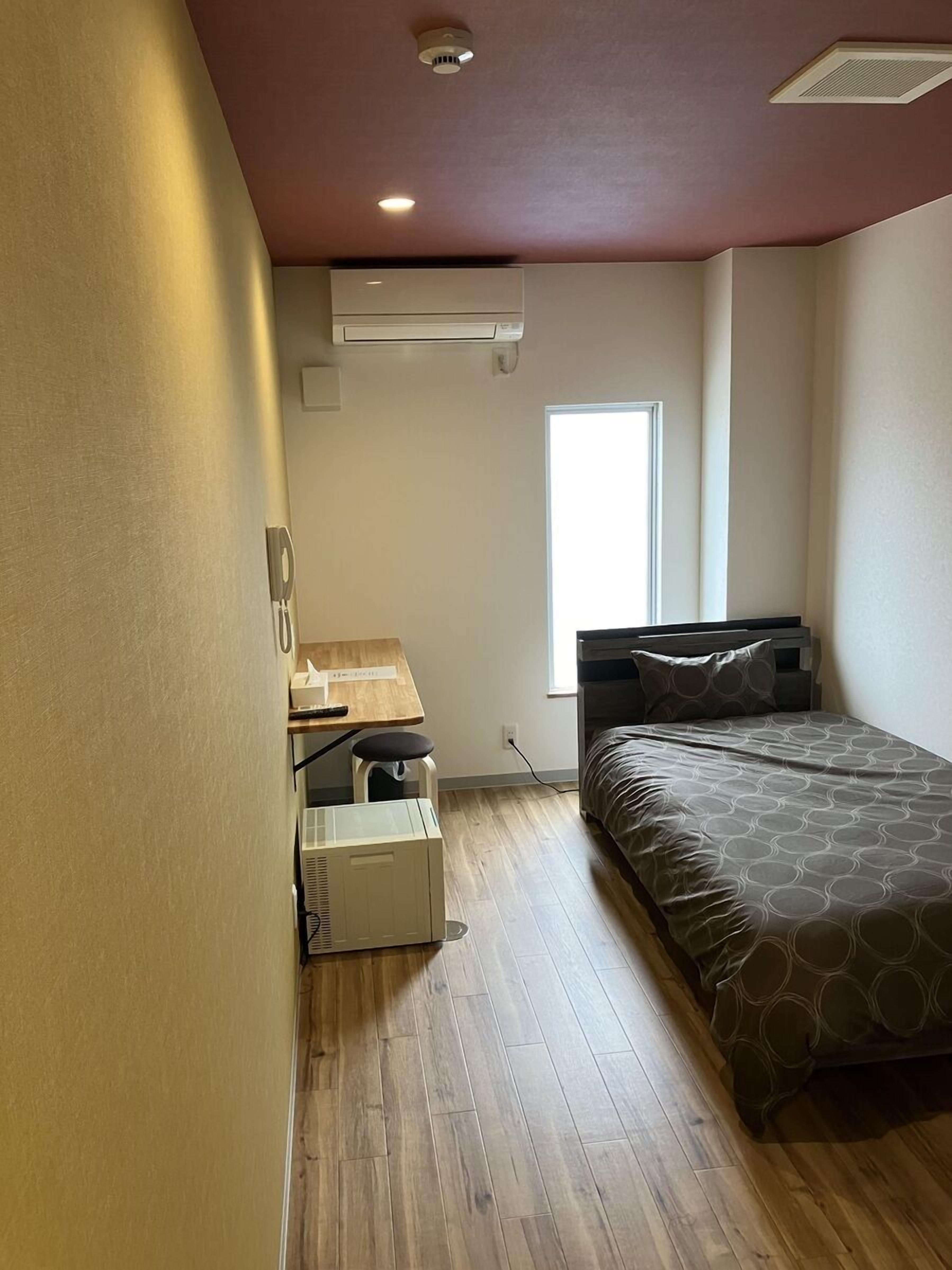 A bedroom with a bed, a desk, a chair, and an air conditioning unit.