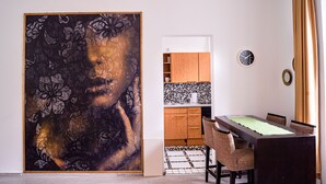 Un coin repas avec une table et des chaises, une cuisine à l’arrière-plan et un grand tableau accroché au mur.