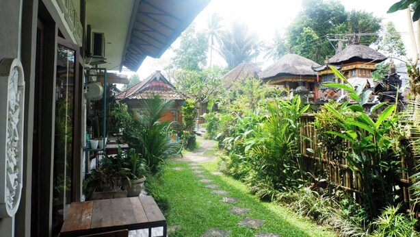 A garden pathway leading to traditional-style buildings with thatched roofs, surrounded by lush greenery and potted plants. - Ramaya House (Tegallalang)
