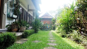 A garden pathway leading to a traditional building with a tiled roof, surrounded by lush greenery and potted plants. - Ramaya House (Tegallalang)