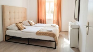 Una cama bien hecha con cabecera, mesita de noche y televisión instalada en la pared.