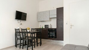 Un espacio habitable compacto con comedor, kitchenette y un sofá gris.