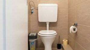 Un inodoro con tanque, un cubo de basura y papel higiénico en la pared.