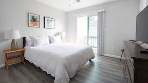 A bedroom with a bed, a nightstand, a ceiling fan, a TV, and a window with a view of the outdoors. - beach. Ocean view. Townhouse (Norfolk)