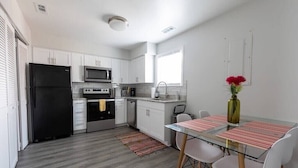 A modern kitchen with white cabinets, a black refrigerator, a microwave, and a sink. There is a dining table with chairs and a vase with flowers. - beach. Ocean view. Townhouse (Norfolk)