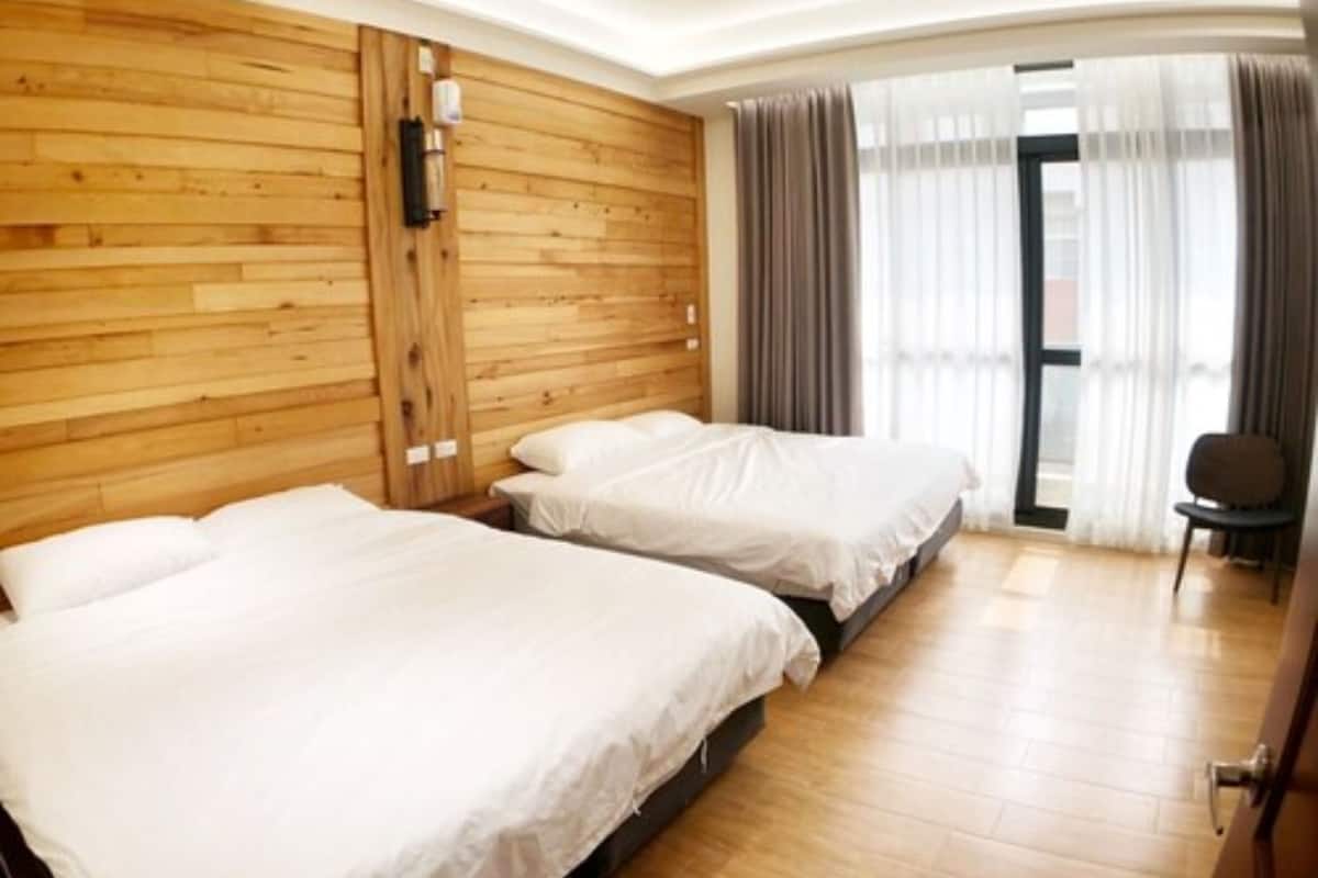 A hotel room with two beds, wooden panel walls, a large window with curtains, and a chair.