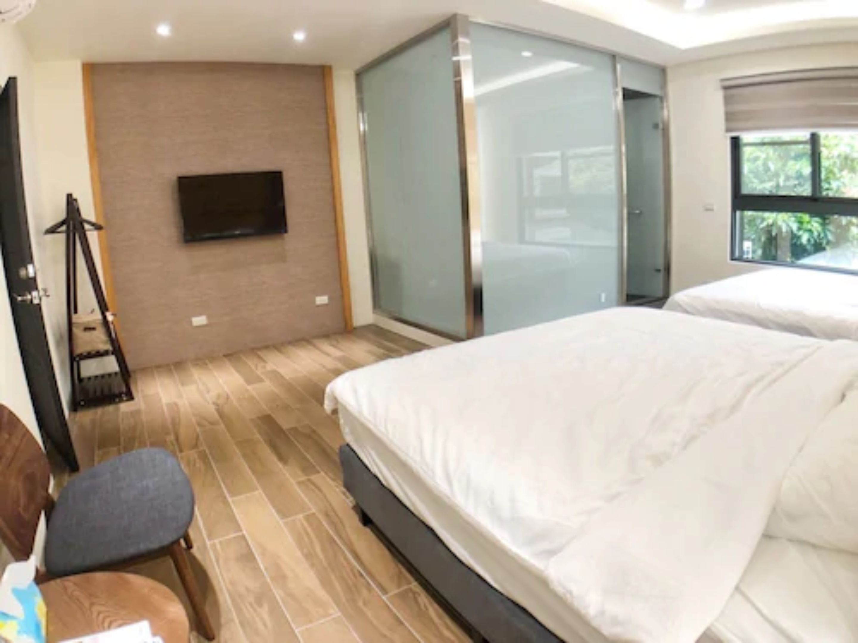 A modern hotel room with a large bed, a TV mounted on the wall, and a sliding glass door leading to a balcony.