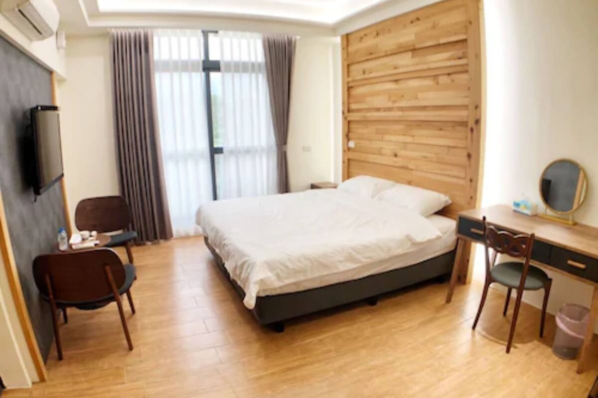 A bedroom with a bed, a desk with a chair, a TV, and a wooden headboard.