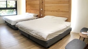 A modern bedroom with two beds, wooden paneling on the wall, and a small table with a chair. - Meet 57 Homestay (Zhuqi)