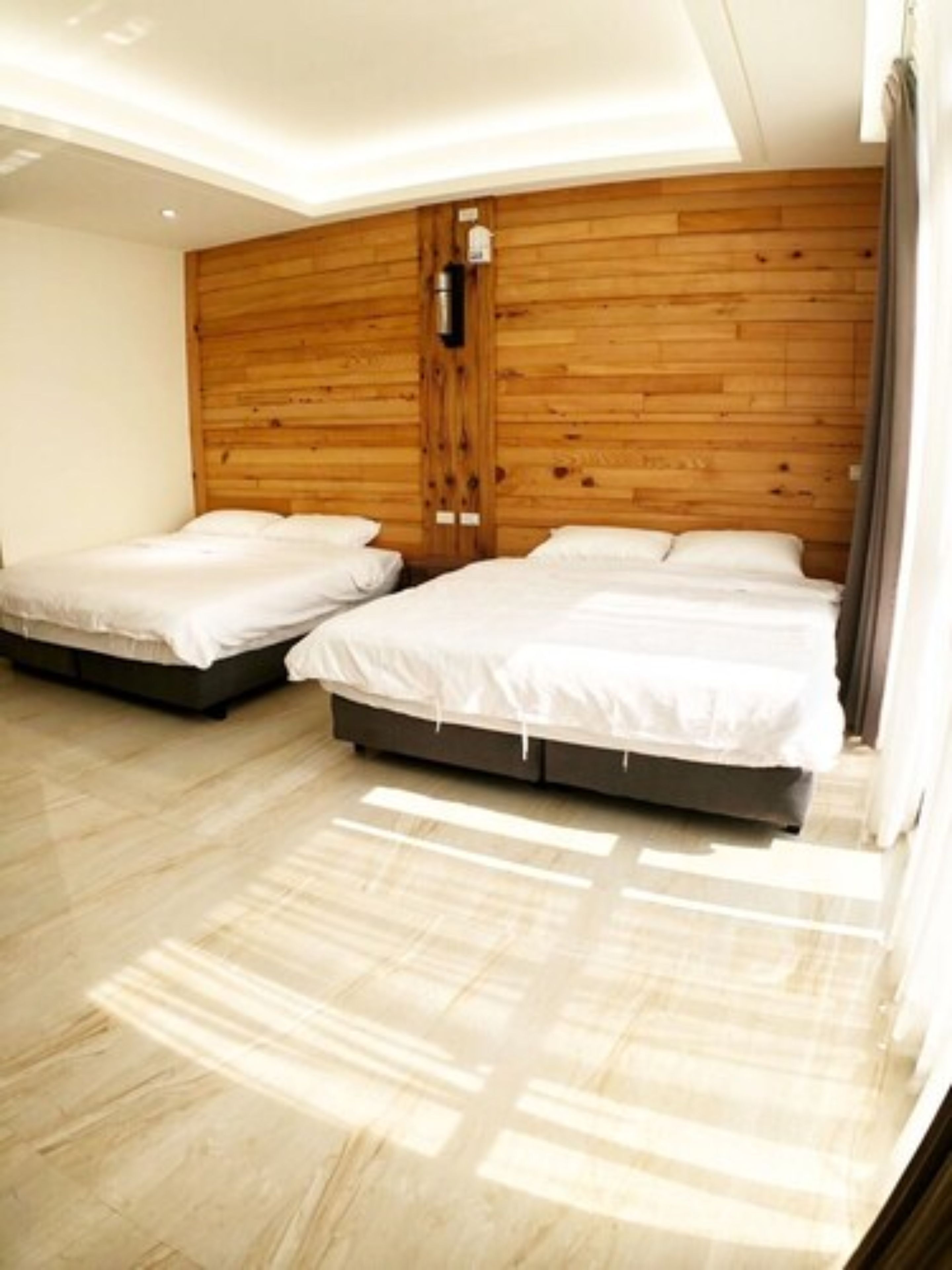 Une chambre moderne avec deux lits, un lambris en bois sur les murs et un plancher de couleur claire.