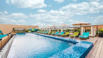 A swimming pool with lounge chairs and umbrellas, surrounded by a wooden deck and a brick wall.