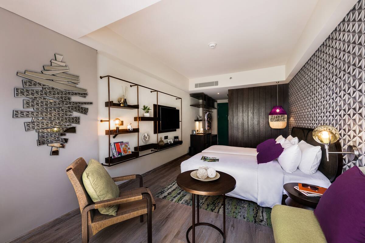 Een moderne hotelkamer met een bed, zithoek, televisie en decoratieve wandkunst.