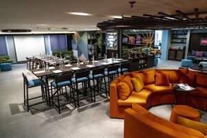 Une salle de conférence moderne, dotée d’une longue table et de chaises, d’un canapé orange vif et de divers objets décoratifs.