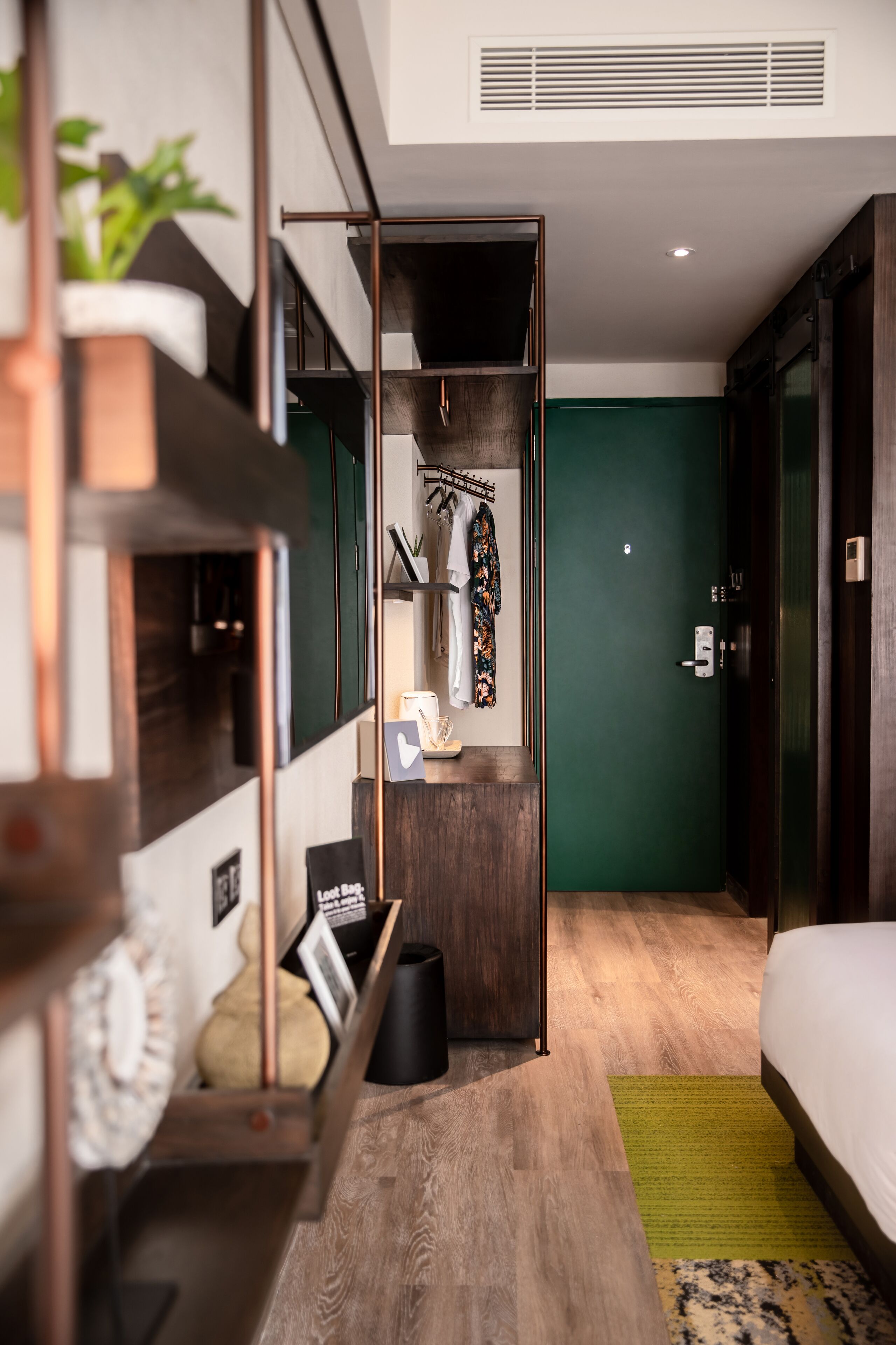 Une chambre d’hôtel moderne avec un lit superposé, un petit bureau avec une lampe, un mur d’accent vert et un lit recouvert d’une couette blanche.