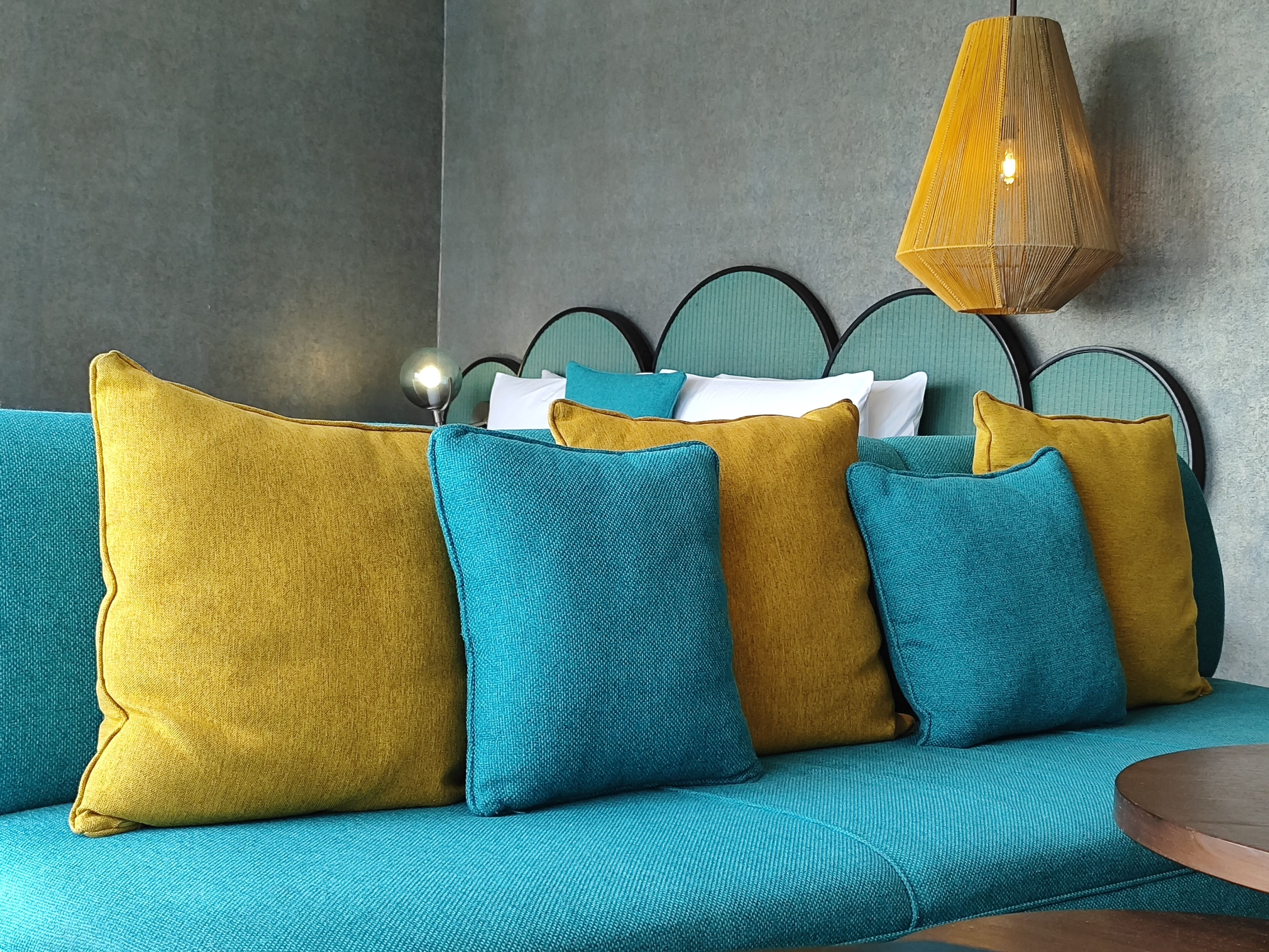 Um sofá azul-esverdeado com almofadas mostarda e azul-esverdeado, uma cabeceira de metal e uma luminária pendente.
