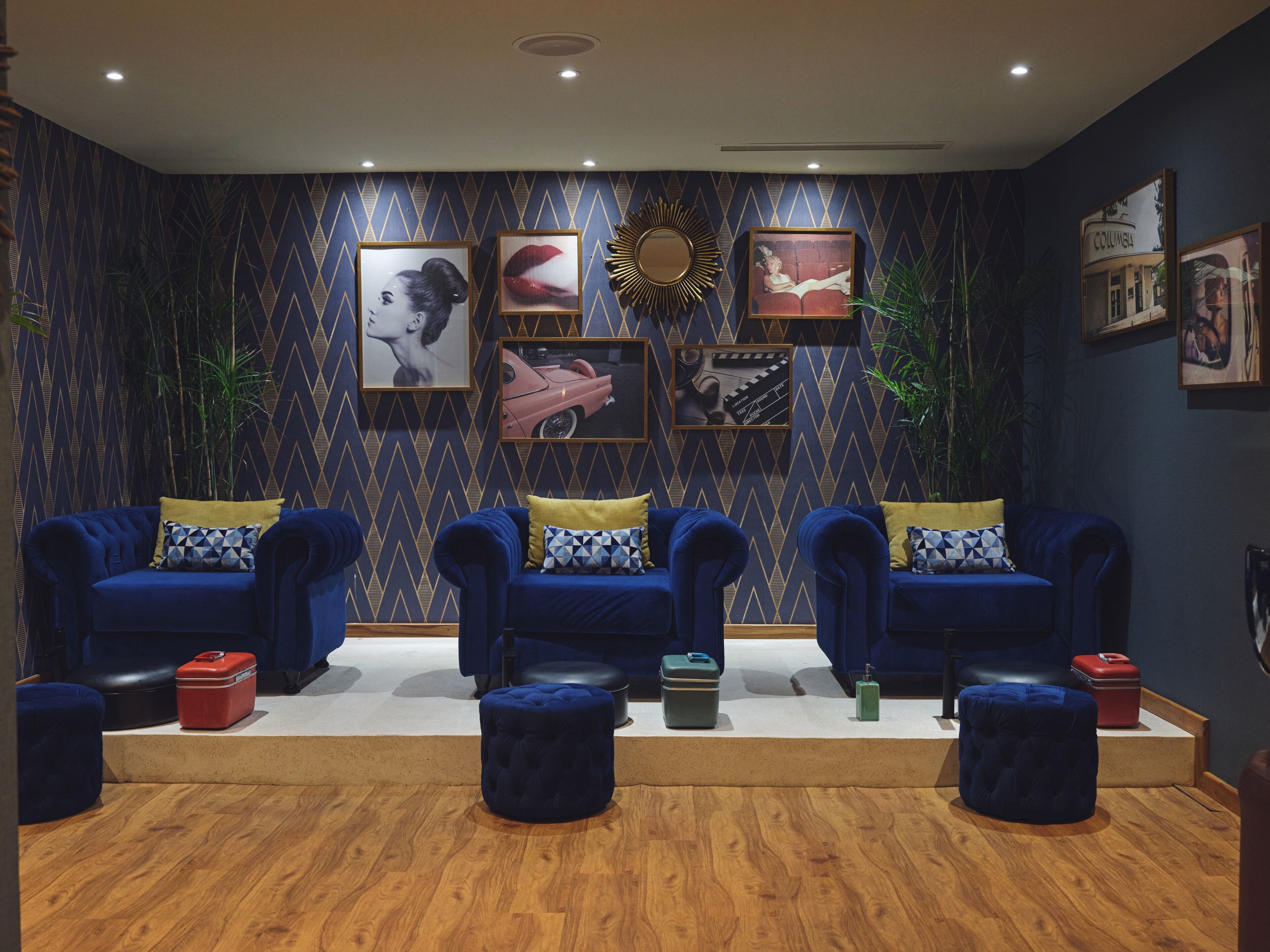 Una habitación con tres sofás azules, piso de madera y una pared decorada con cuadros enmarcados.