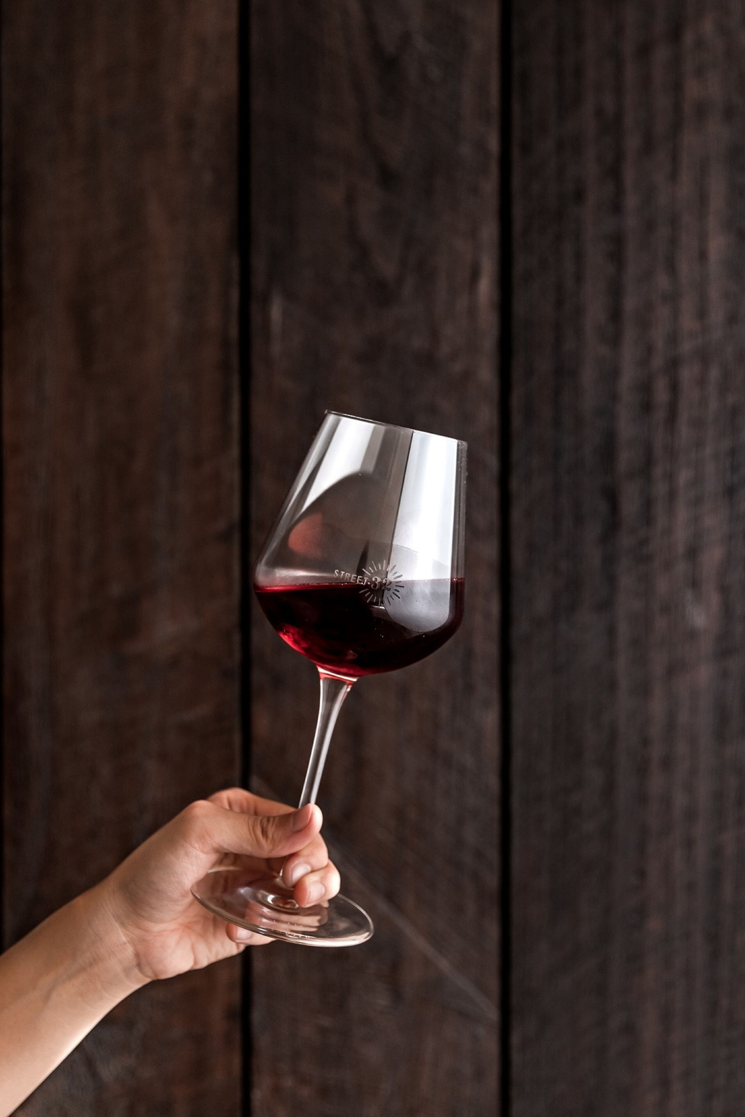 Une main tenant un verre à vin contenant un liquide sombre, sur un fond en bois.
