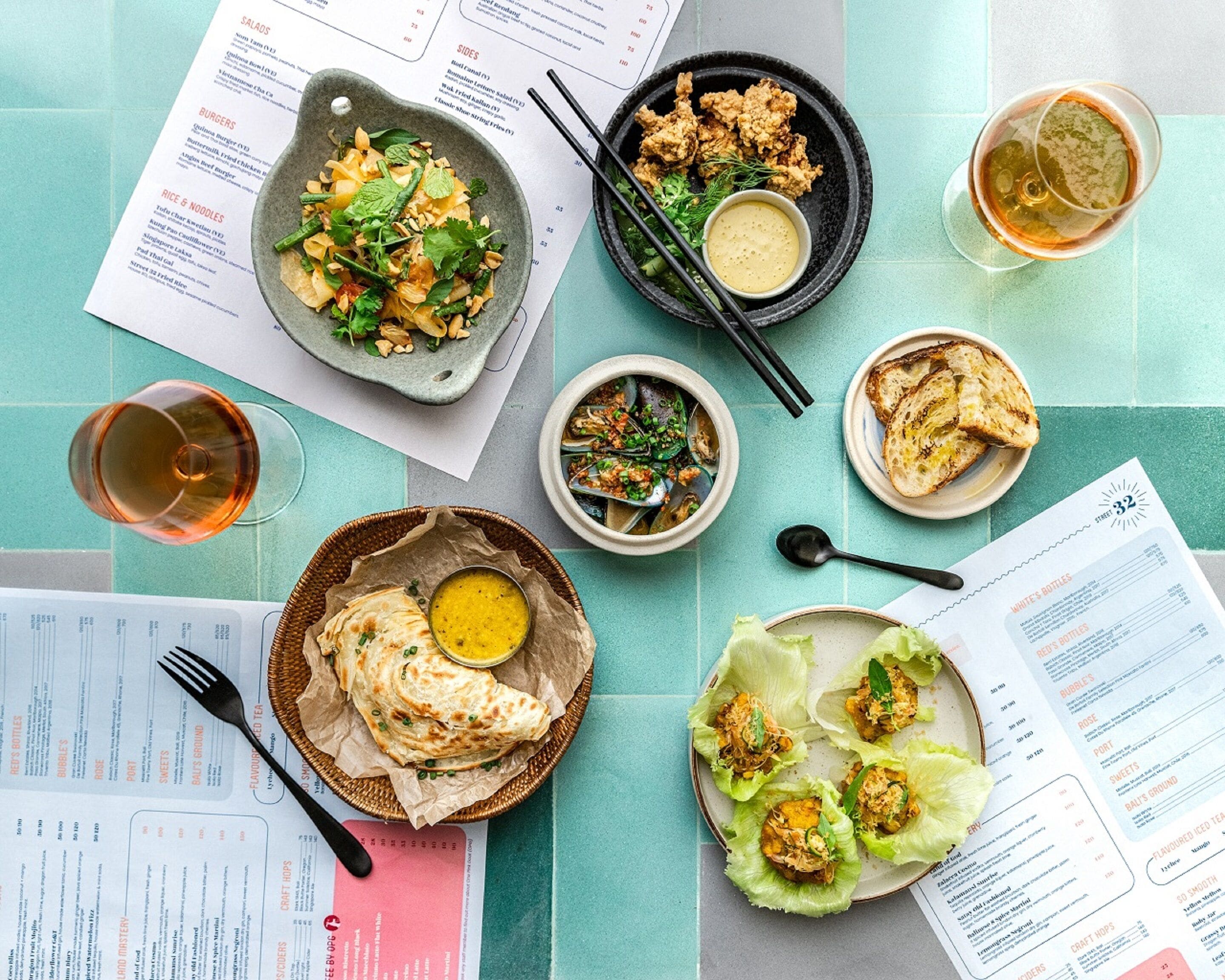 A table with various dishes, including salads, noodles, and bread, along with menus and a glass of drink.